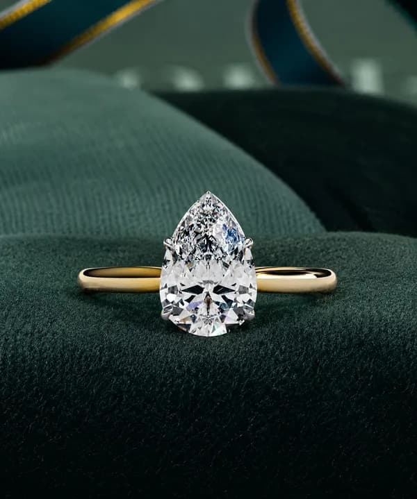 Pear cut lab grown diamond cathedral solitaire engagement ring in yellow gold on green velvet