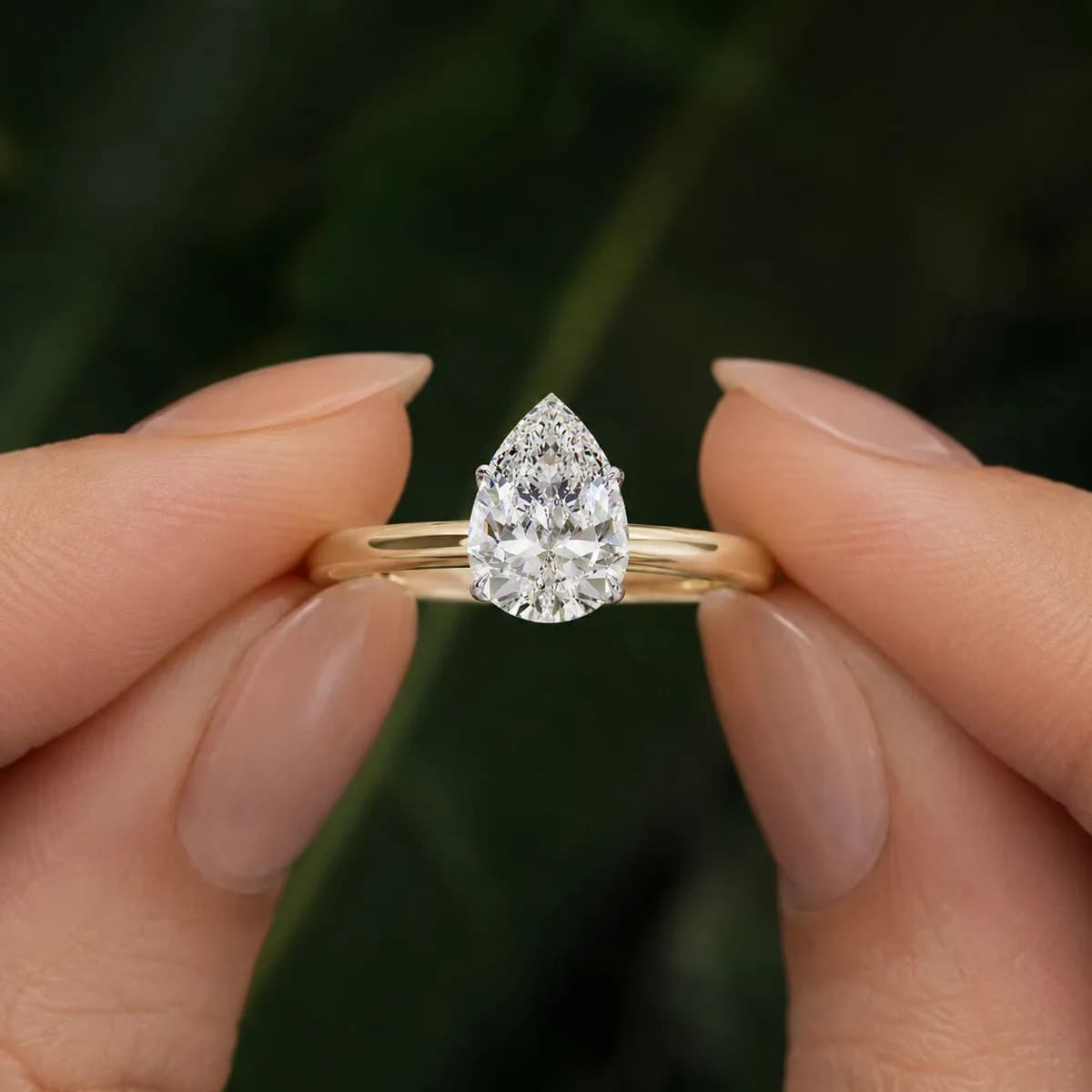 Pear cut lab grown diamond cathedral solitaire engagement ring in yellow gold held between fingertips
