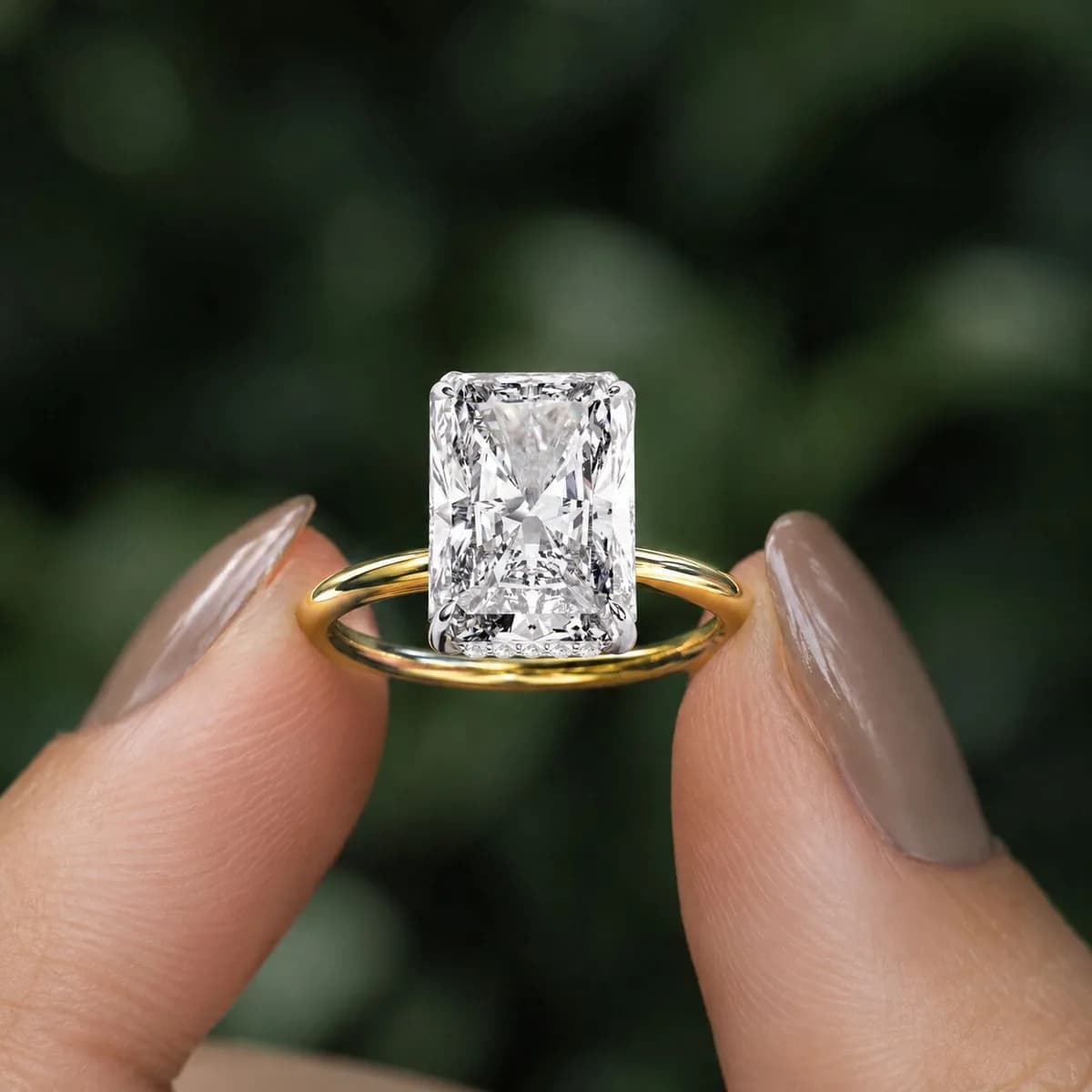 Radiant cut lab grown diamond hidden halo solitaire engagement ring in yellow gold held between fingertips