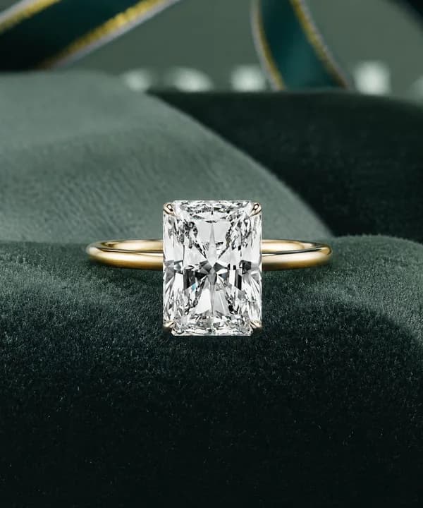 Radiant cut lab grown diamond hidden halo solitaire engagement ring in yellow gold on a green velvet cushion
