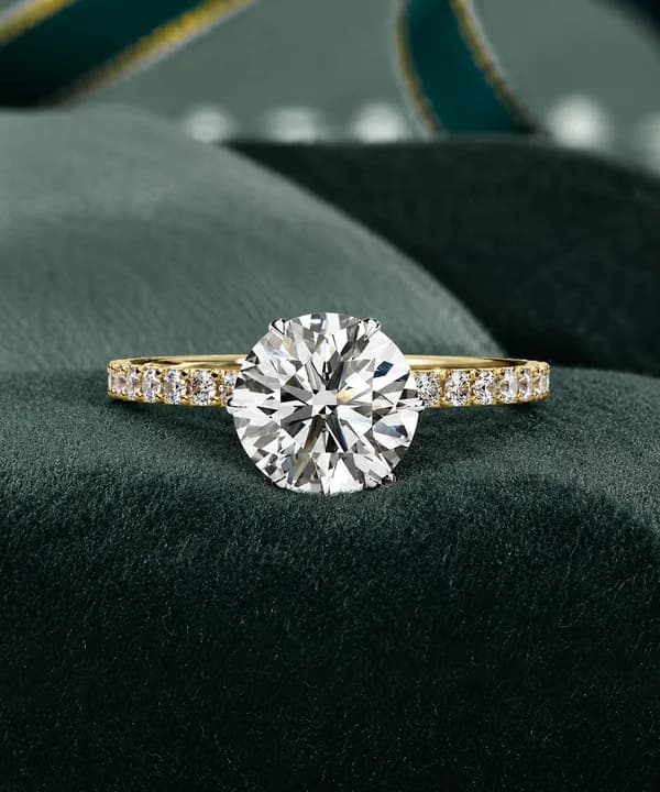 Round lab grown diamond hidden halo pavé engagement ring in yellow gold resting on a green velvet cushion