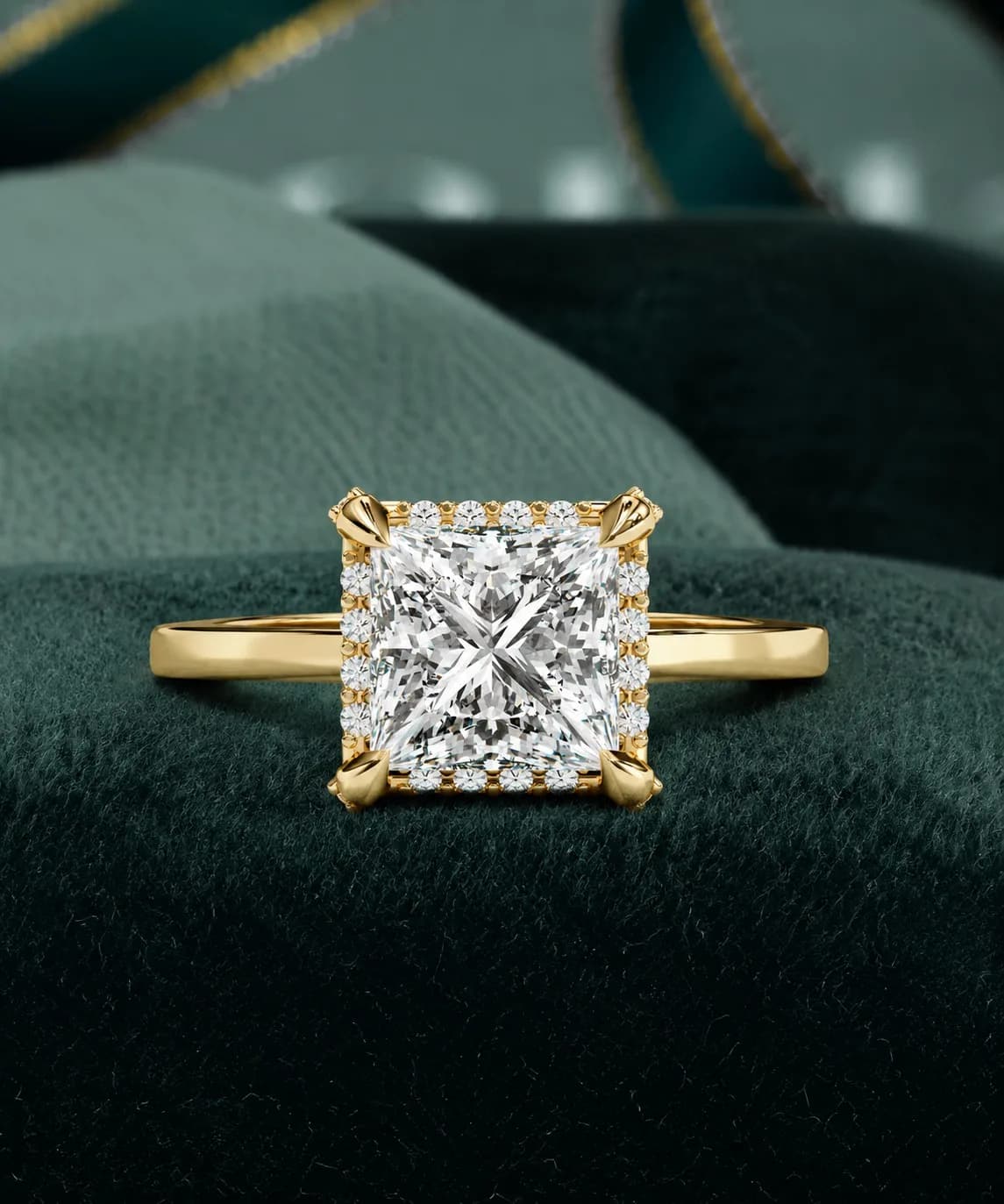 Princess cut lab grown diamond low halo engagement ring in yellow gold on a green velvet cushion
