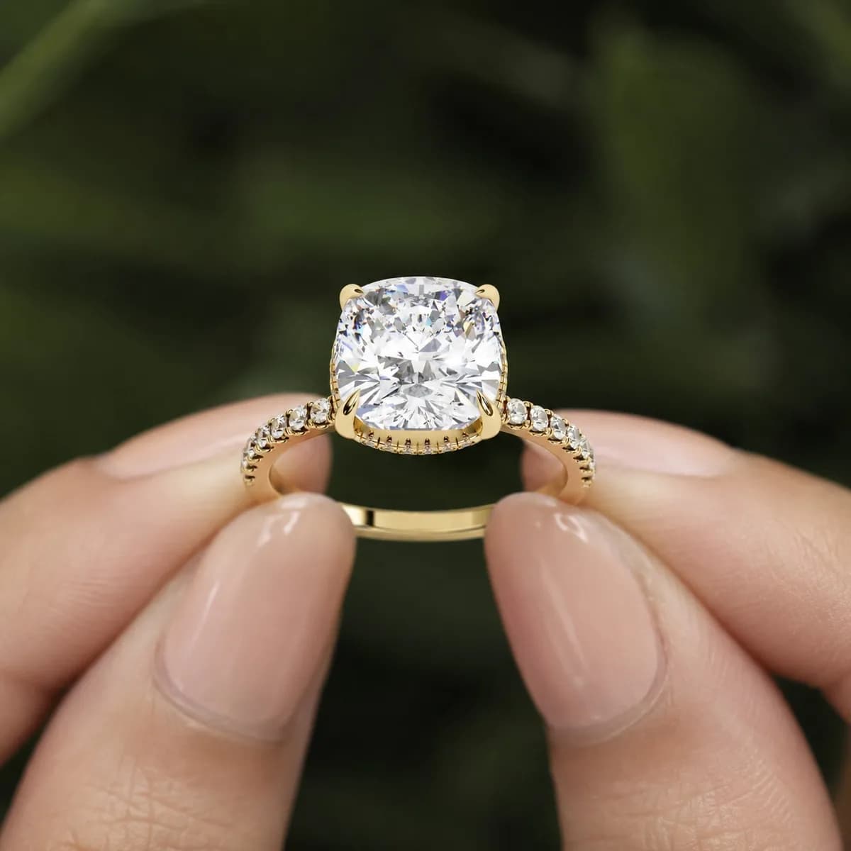 Cushion cut lab grown diamond hidden halo engagement ring in yellow gold held between fingertips