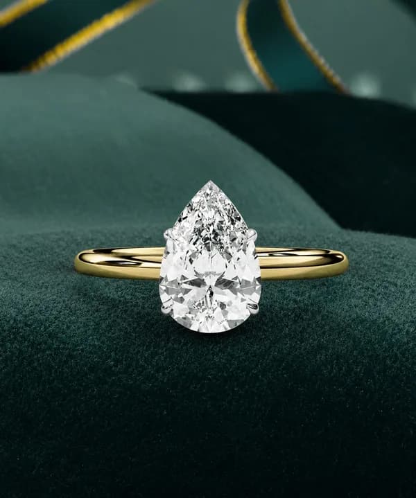 Pear cut lab grown diamond solitaire engagement ring in yellow gold resting on green velvet