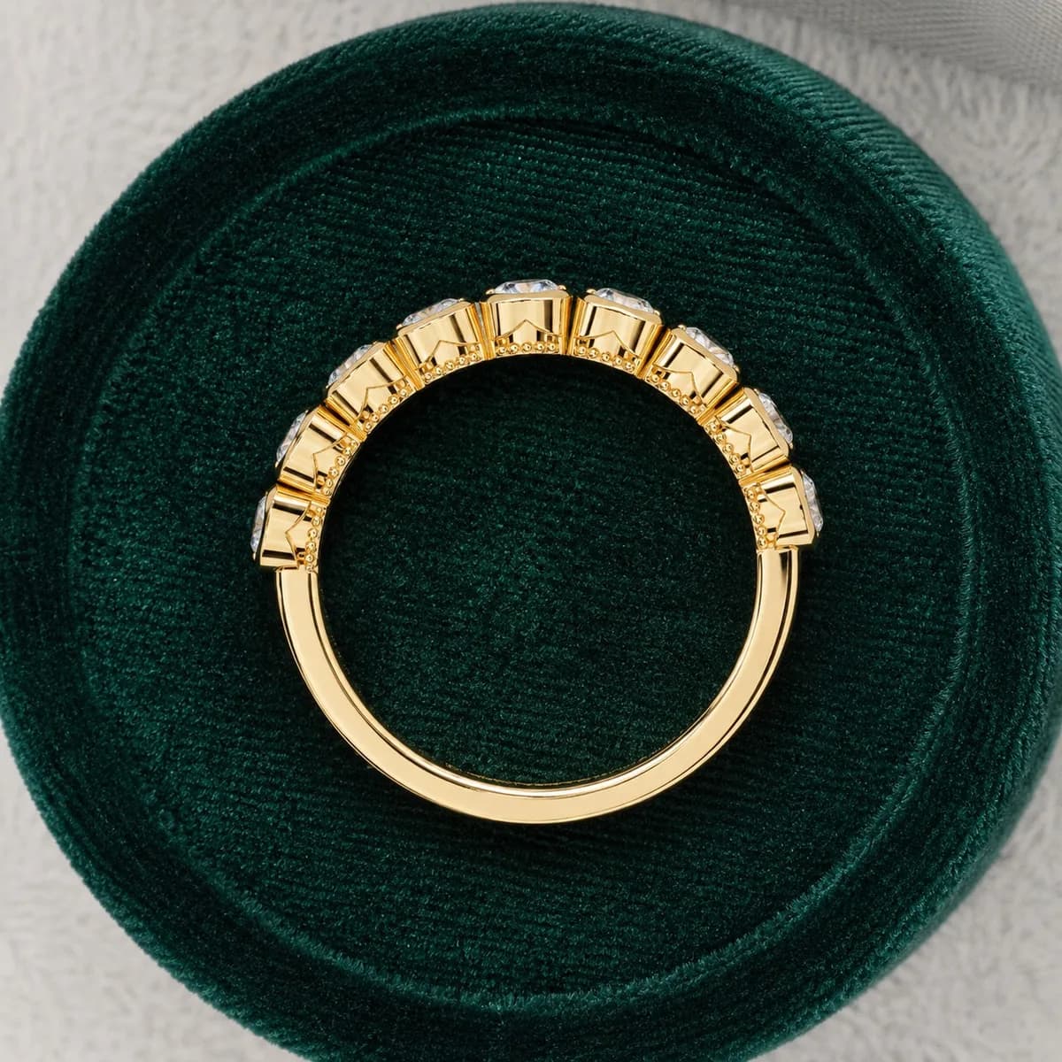 Round lab grown diamond bezel set half eternity wedding band in yellow gold in a green velvet ring box