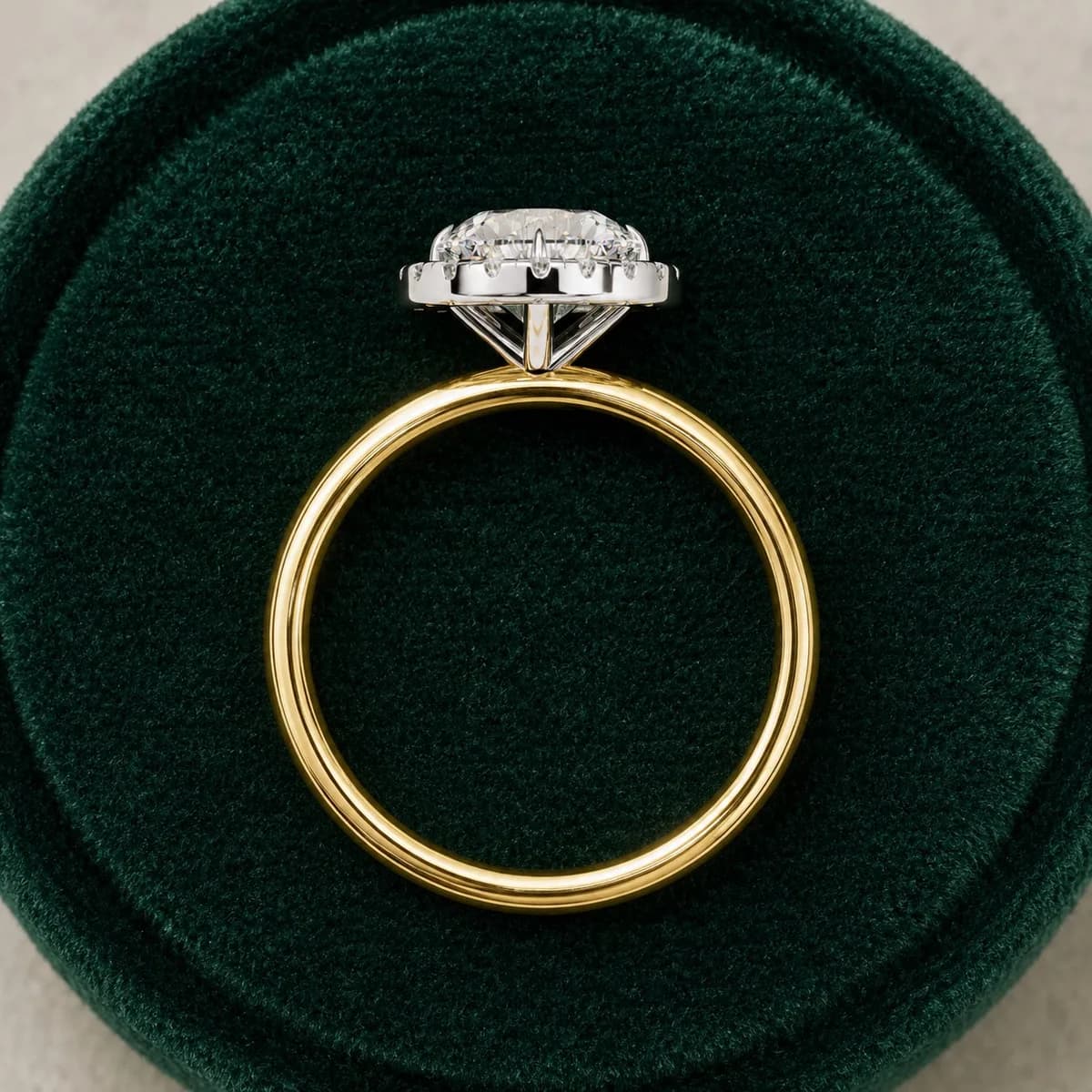 Round lab grown diamond halo engagement ring with plain band in yellow gold standing in a green velvet ring box