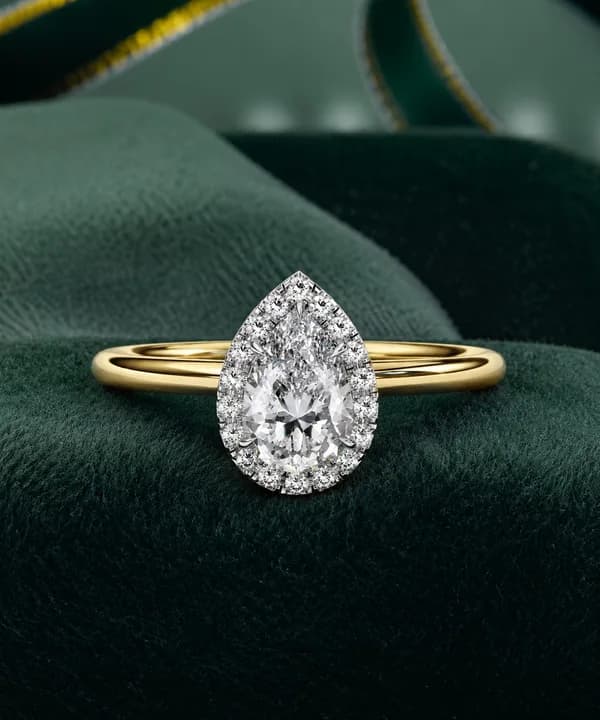 Pear cut lab grown diamond halo engagement ring in yellow gold resting on green velvet