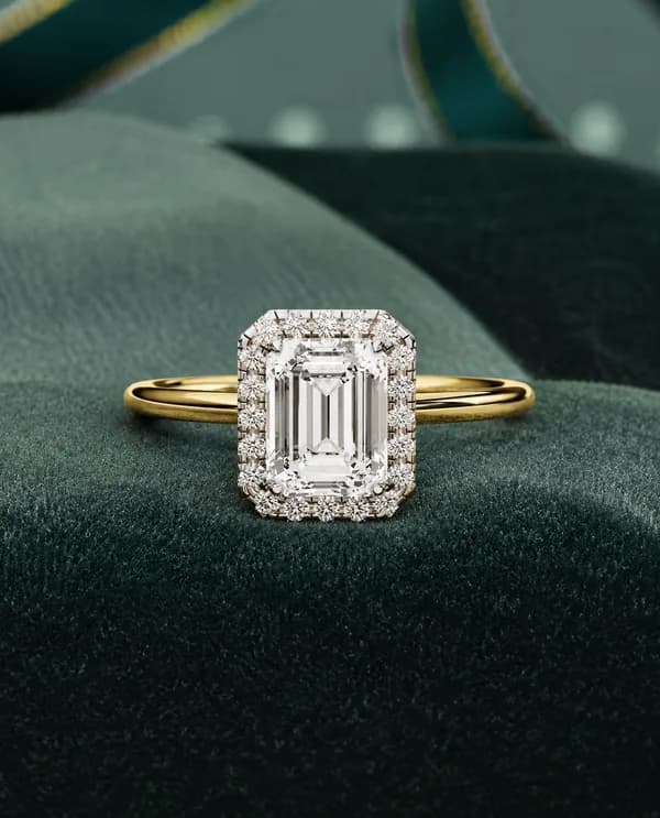 Emerald cut lab grown diamond halo engagement ring in yellow gold resting on green velvet