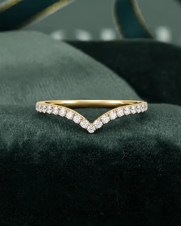 Round lab grown diamond chevron pavé wedding band in yellow gold on a green velvet cushion