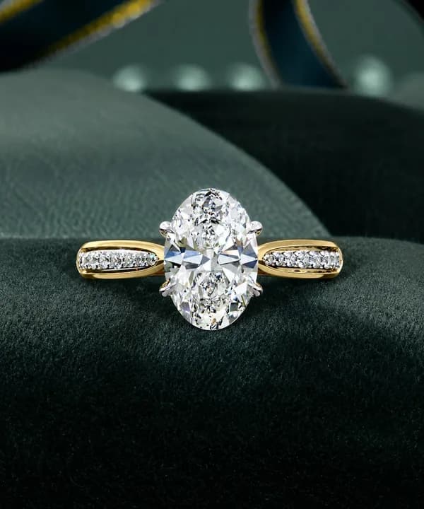 Oval lab grown diamond cathedral pavé engagement ring in yellow gold resting on green velvet