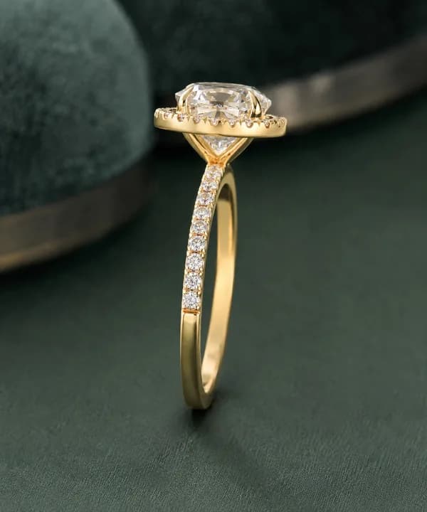 Cushion cut lab grown diamond halo engagement ring in yellow gold standing on green velvet, side view
