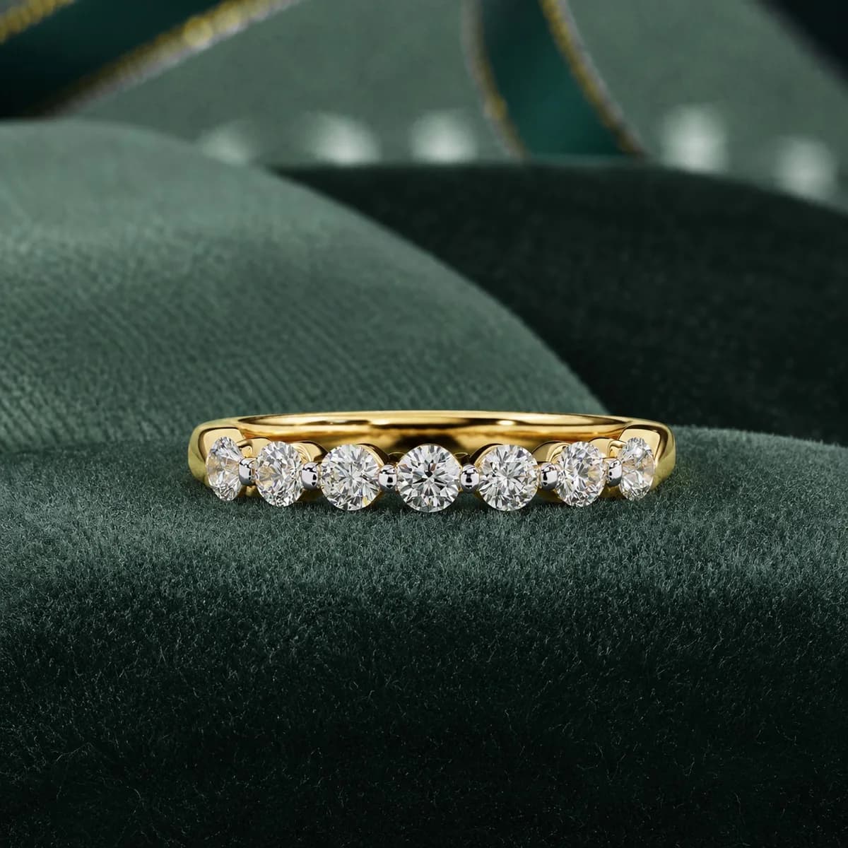 Round lab grown diamond seven-stone wedding band in yellow gold resting on green velvet