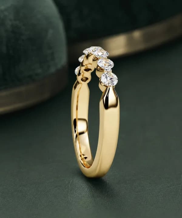 Round lab grown diamond seven-stone wedding band in yellow gold, side view on green velvet
