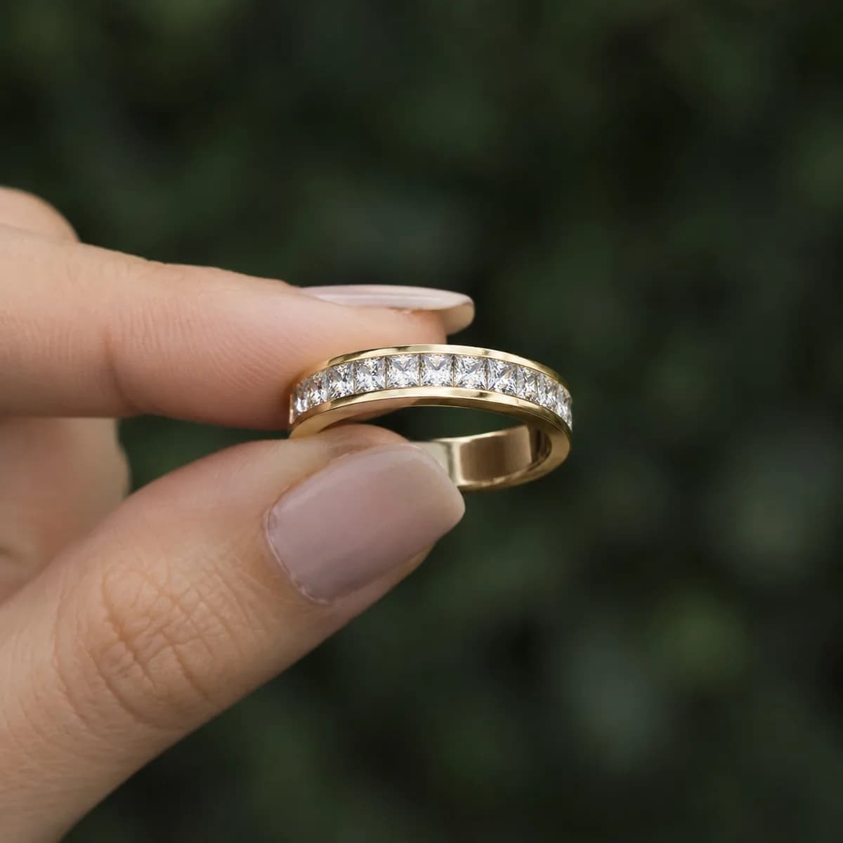 Princess cut lab grown diamond channel-set half eternity band in yellow gold held between fingertips