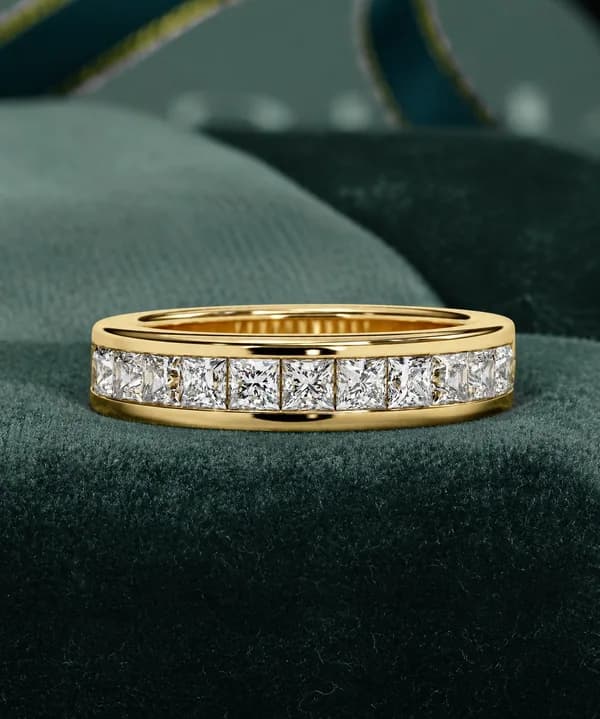 Princess cut lab grown diamond channel-set half eternity band in yellow gold resting on green velvet