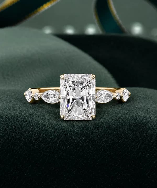 Radiant cut lab grown diamond engagement ring with marquise accents in yellow gold on a green velvet cushion