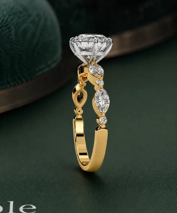 Round lab grown diamond engagement ring with marquise side stones in yellow gold on green velvet, side view