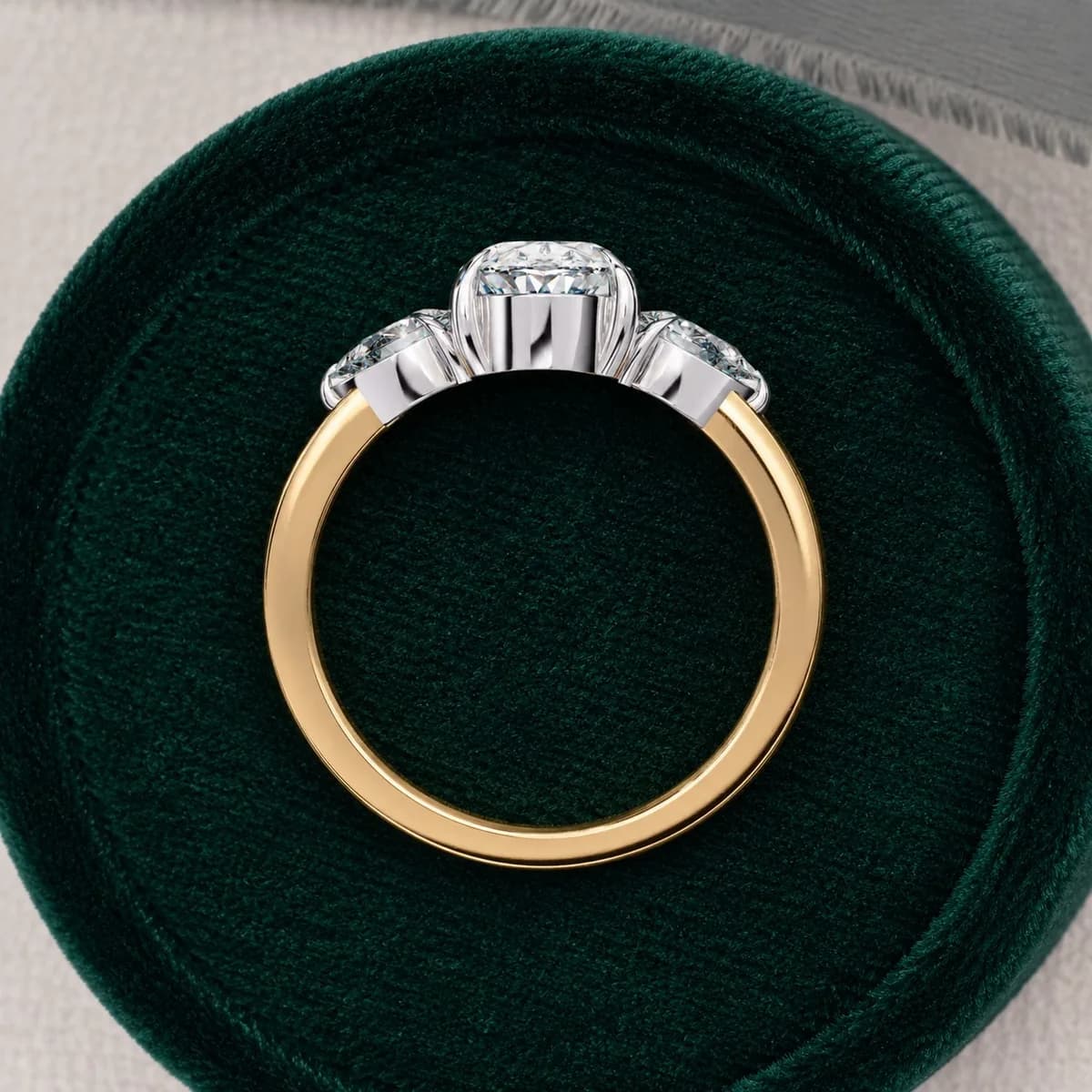 Oval lab grown diamond three-stone engagement ring with pear side stones in yellow gold in a green velvet ring box