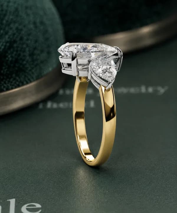 Pear cut lab grown diamond three-stone engagement ring in yellow gold on green velvet, side view