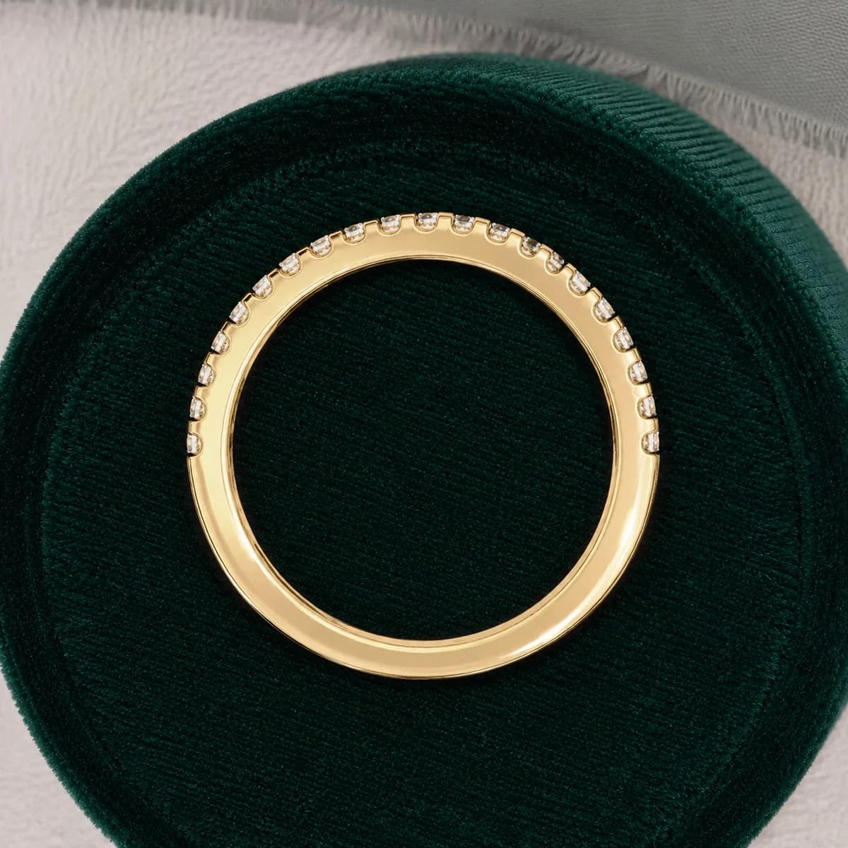 Round lab grown diamond pavé half eternity band in yellow gold standing in a green velvet ring box
