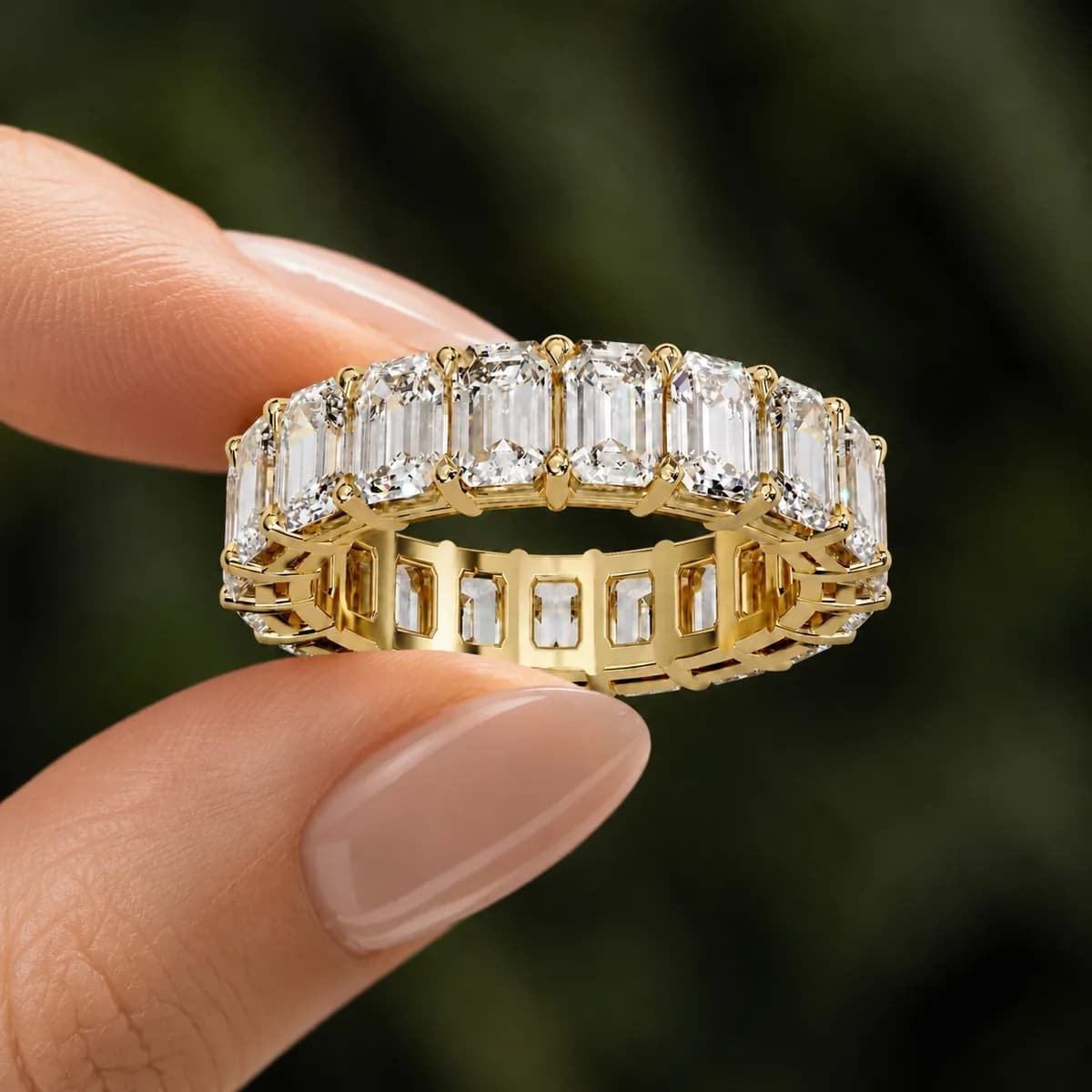 Emerald cut lab grown diamond full eternity wedding band in yellow gold held between fingertips