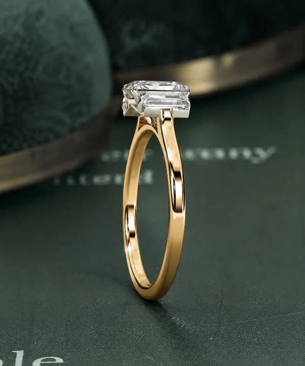 Emerald cut lab grown diamond three-stone engagement ring in yellow gold on green velvet, side view