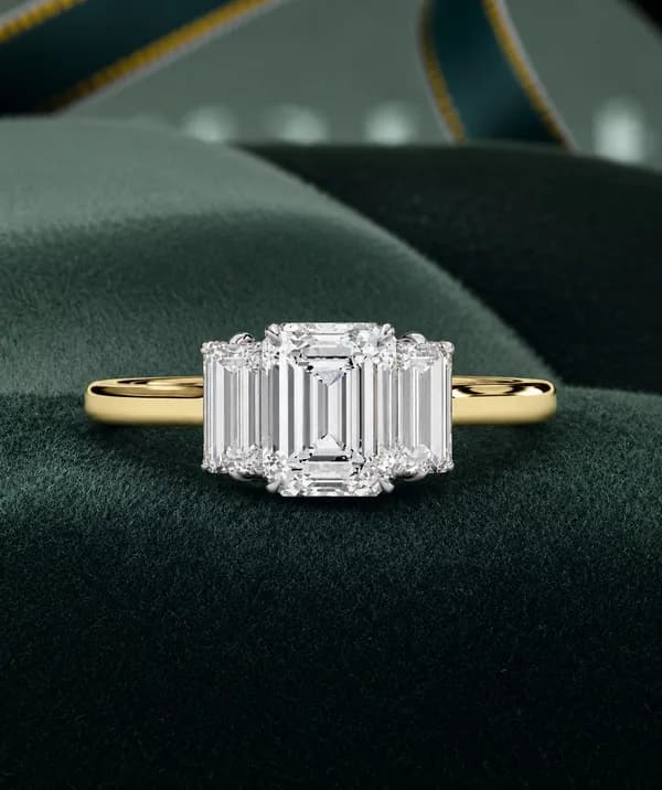 Emerald cut lab grown diamond three-stone engagement ring in yellow gold on green velvet