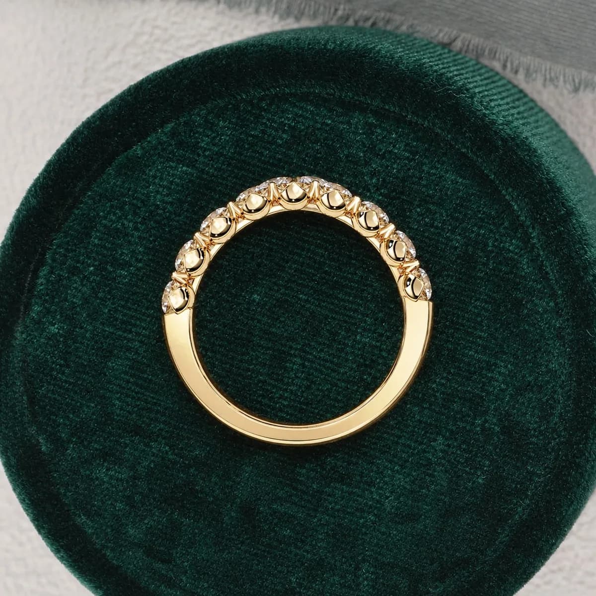 Round lab grown diamond half eternity wedding band in yellow gold standing in a green velvet ring box