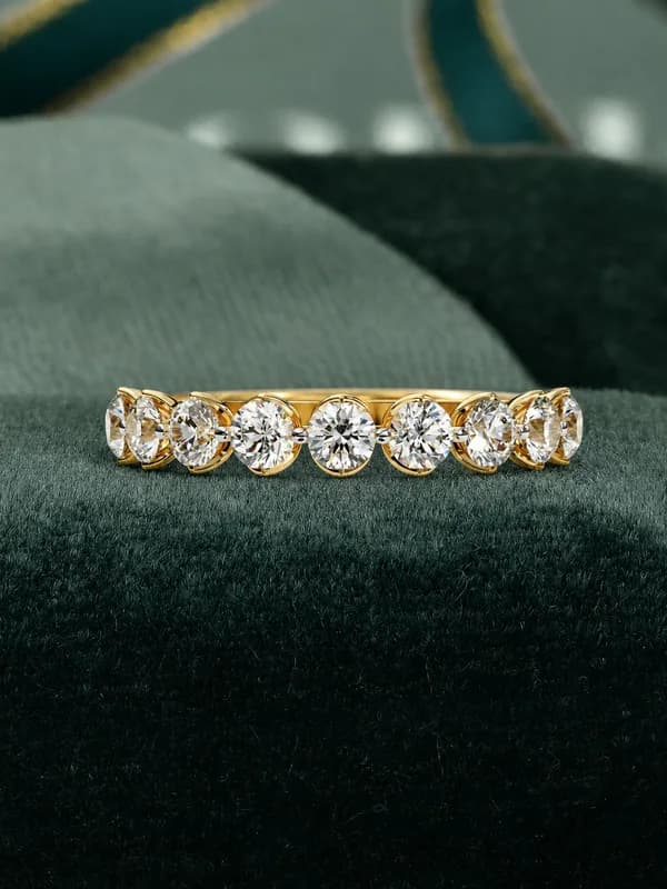 Round lab grown diamond half eternity wedding band in yellow gold resting on green velvet