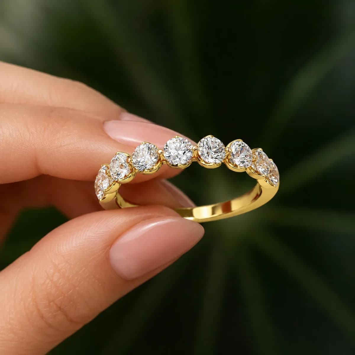 Round lab grown diamond half eternity wedding band in yellow gold held between fingertips