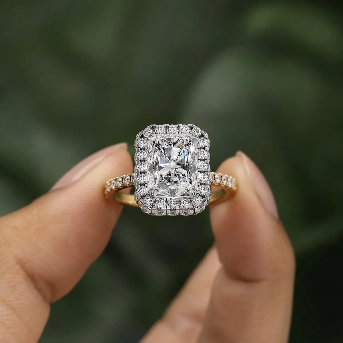 Radiant cut lab grown diamond halo engagement ring with pavé band in yellow gold held between fingertips