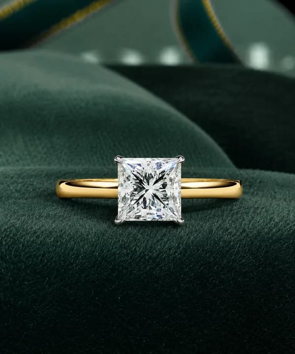 Princess cut lab grown diamond cathedral solitaire engagement ring in yellow gold on a green velvet cushion