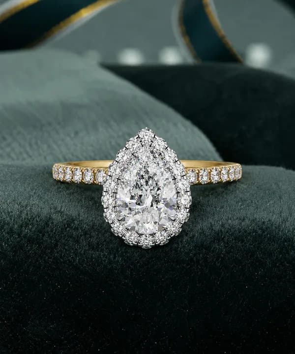 Pear cut lab grown diamond halo engagement ring with pavé band in yellow gold resting on green velvet