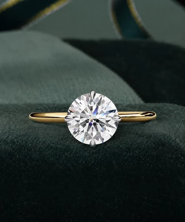 Round lab grown diamond compass prong solitaire engagement ring in yellow gold on a green velvet cushion