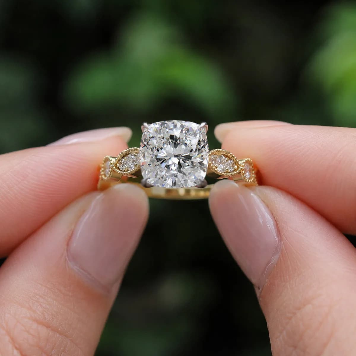 Cushion cut lab grown diamond vintage milgrain engagement ring in yellow gold held between fingertips