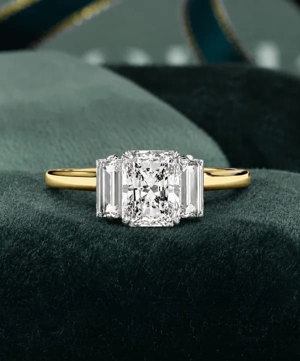 Radiant cut lab grown diamond three-stone engagement ring in yellow gold resting on green velvet