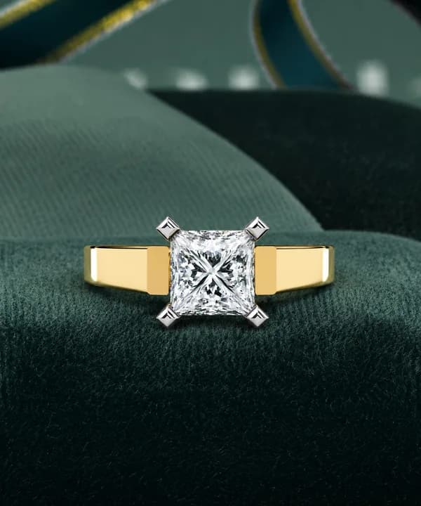 Princess cut lab grown diamond cathedral solitaire engagement ring in yellow gold resting on green velvet
