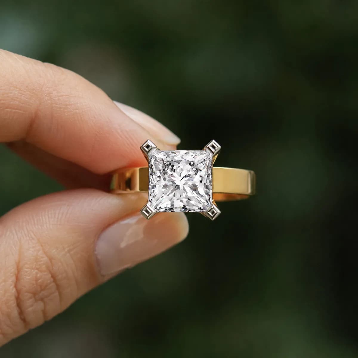 Princess cut lab grown diamond cathedral solitaire engagement ring in yellow gold held between fingertips