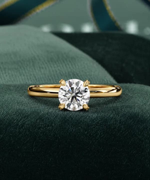 Round lab grown diamond pavé claw solitaire engagement ring in yellow gold resting on green velvet