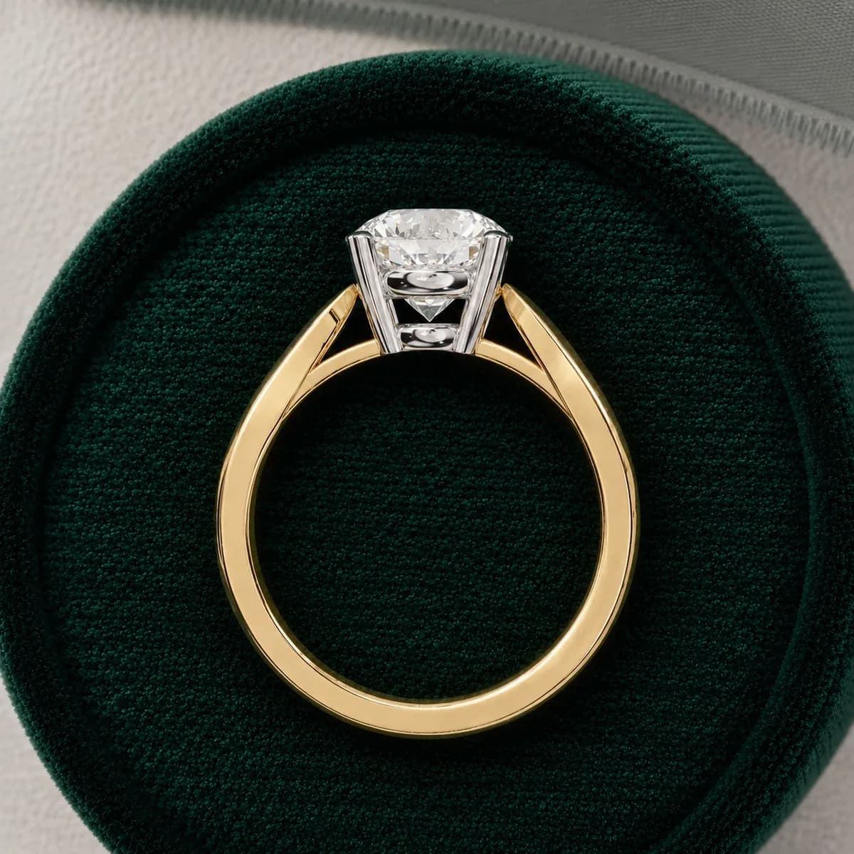 Round lab grown diamond four-claw cathedral solitaire engagement ring in yellow gold in a green velvet ring box