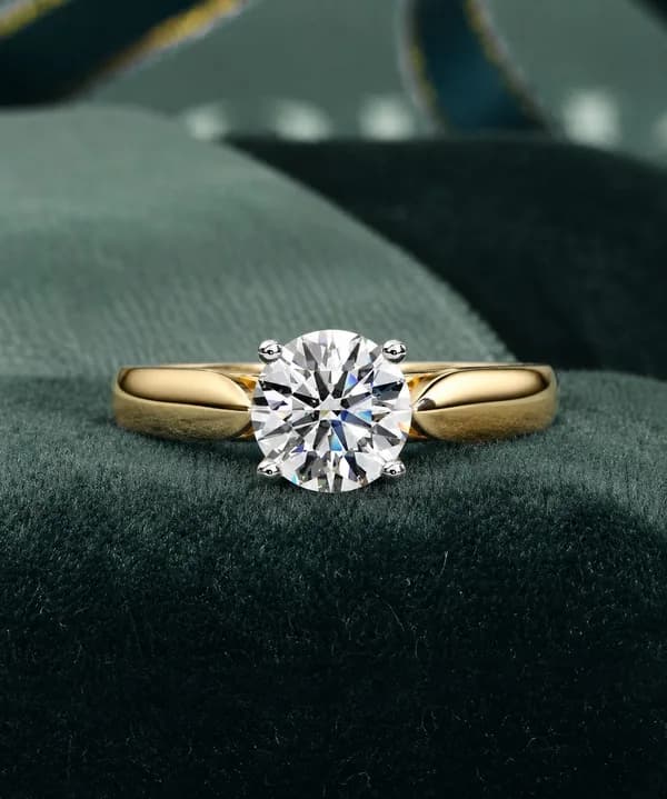 Round lab grown diamond four-claw cathedral solitaire engagement ring in yellow gold on green velvet