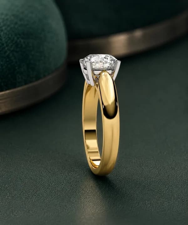 Round lab grown diamond four-claw cathedral solitaire engagement ring in yellow gold on green velvet