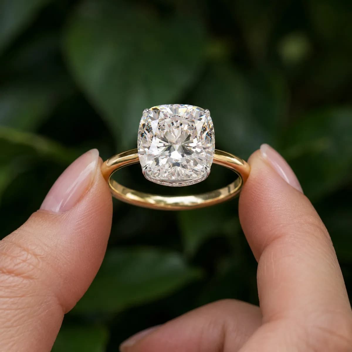 Cushion cut lab grown diamond hidden halo solitaire in yellow gold held between fingertips