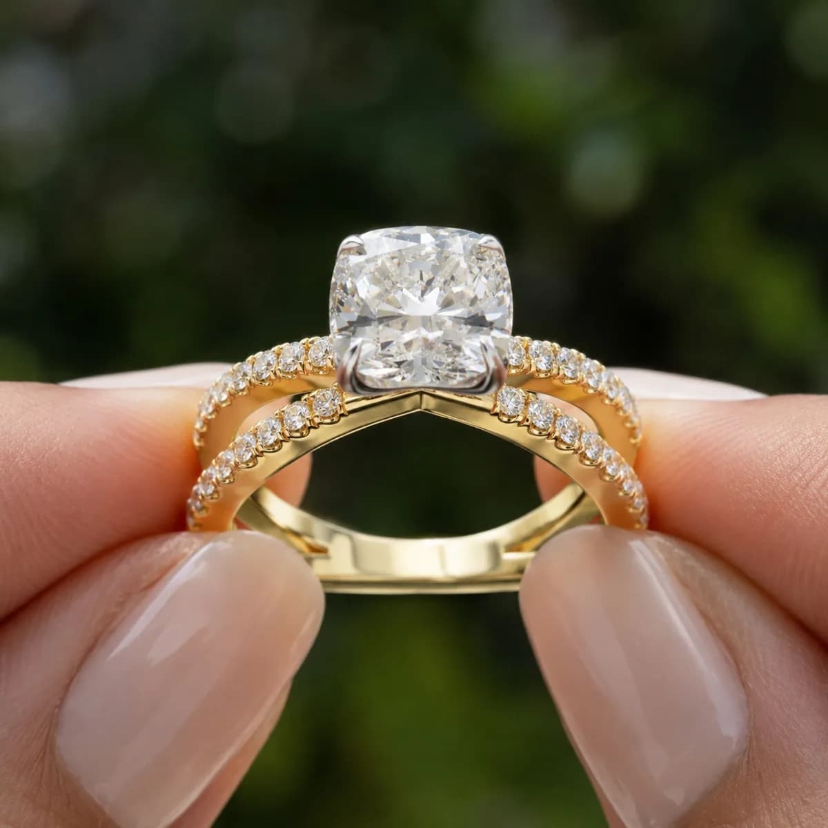 Cushion cut lab grown diamond crossover pavé engagement ring in yellow gold held between fingertips