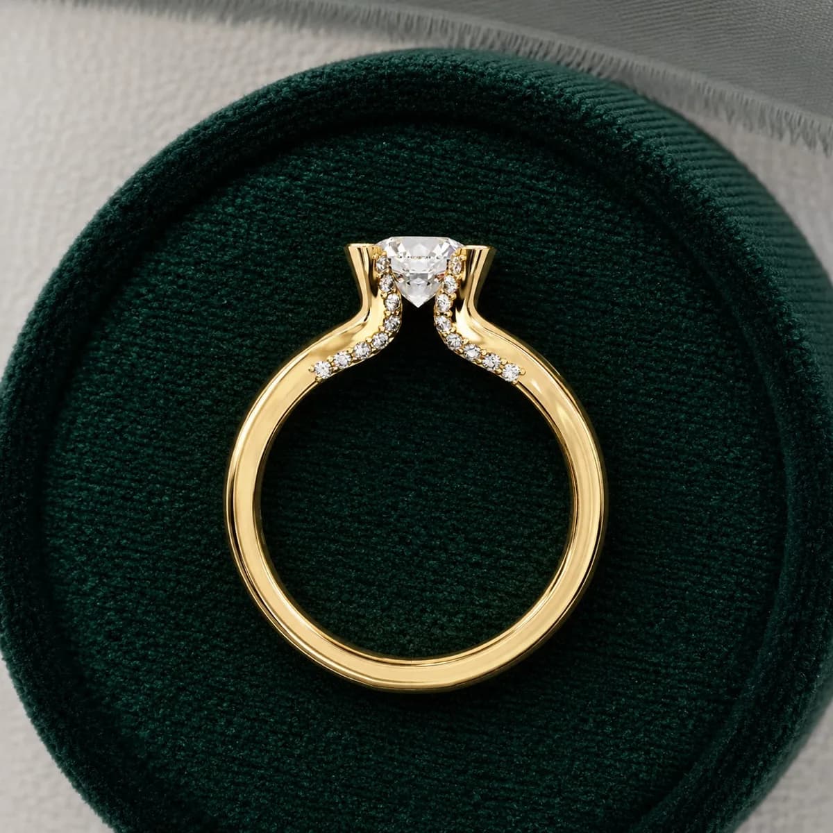 Round lab grown diamond split shank engagement ring with petal claws in yellow gold standing in a green velvet ring box