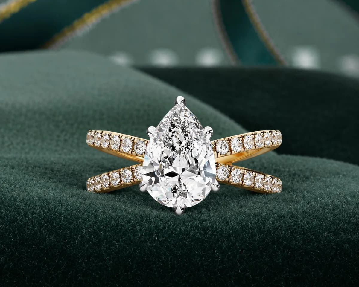 Pear cut lab grown diamond crossover split shank engagement ring in yellow gold on green velvet