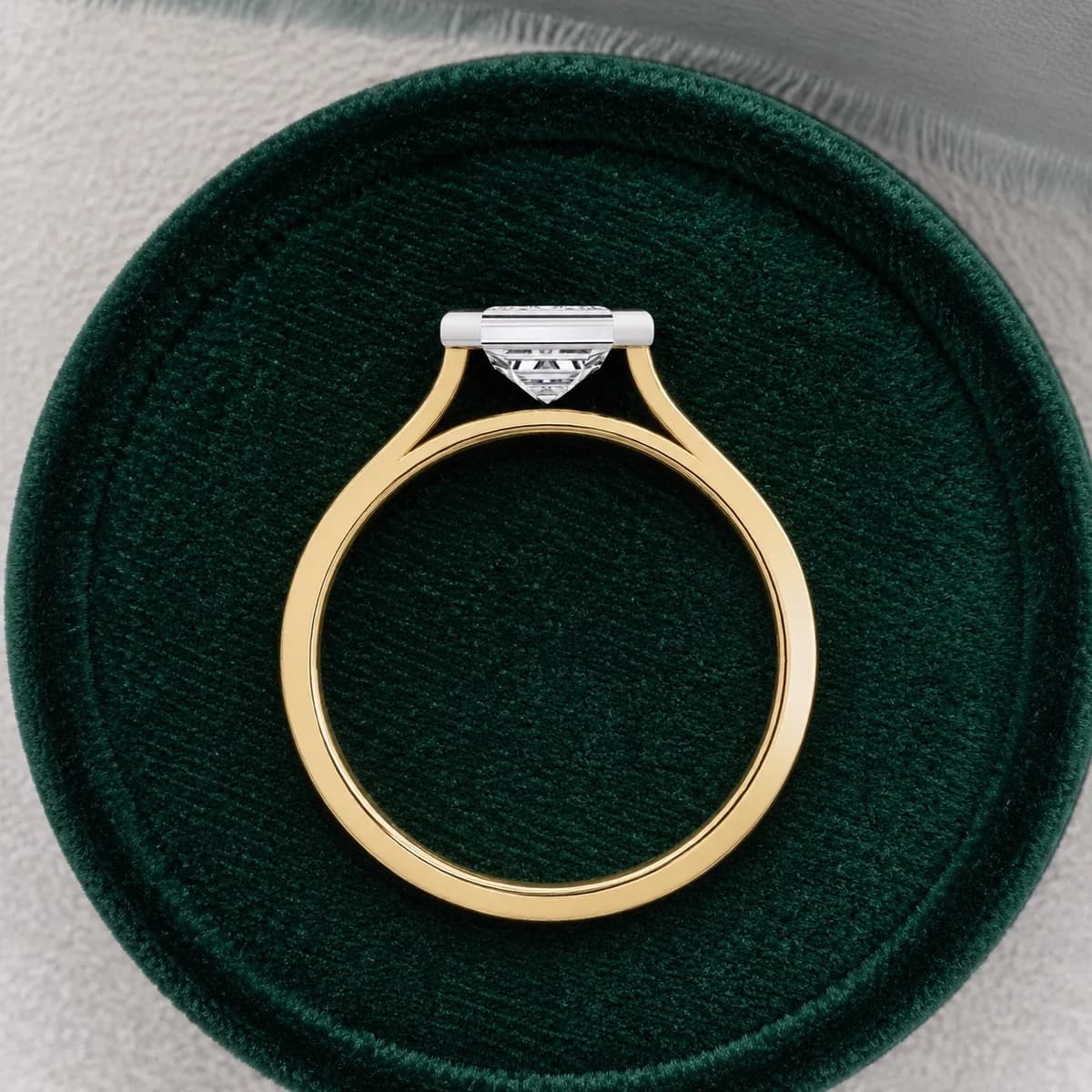 Emerald cut lab grown diamond bezel solitaire engagement ring in yellow gold standing in a green velvet ring box