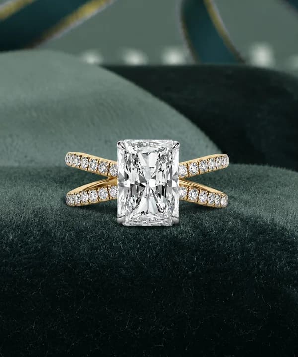 Radiant cut lab grown diamond crossover split shank ring in yellow gold resting on green velvet