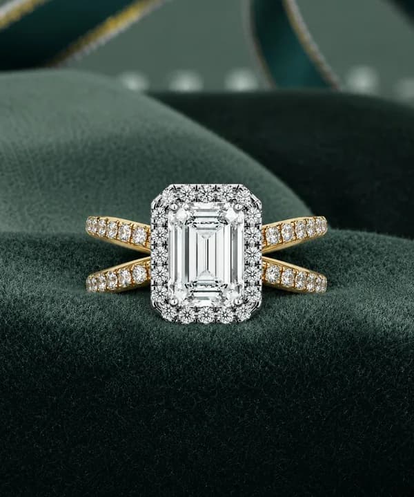 Emerald cut lab grown diamond halo criss-cross pavé engagement ring in yellow gold resting on green velvet
