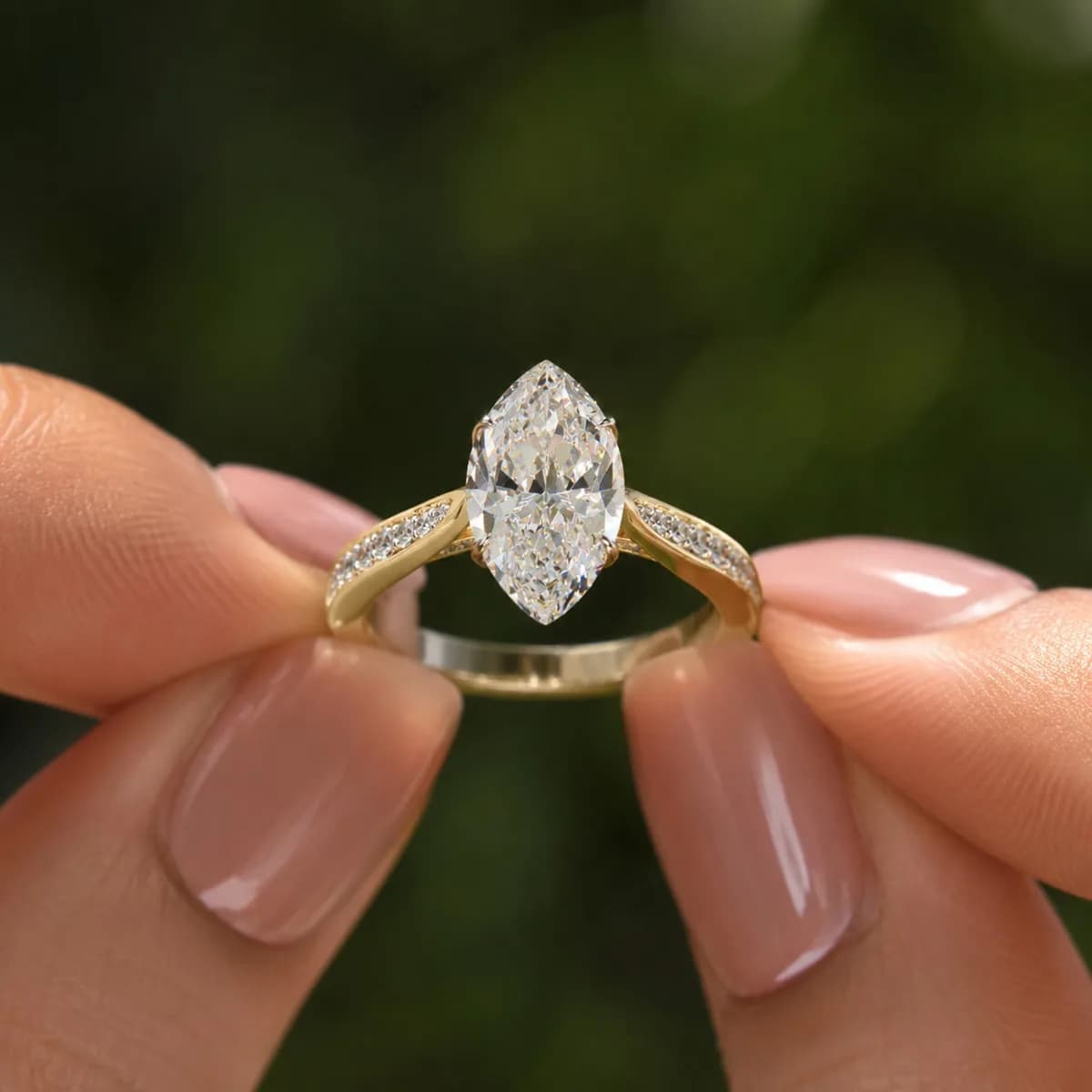 Marquise lab grown diamond cathedral engagement ring with pavé shoulders in yellow gold held between fingertips